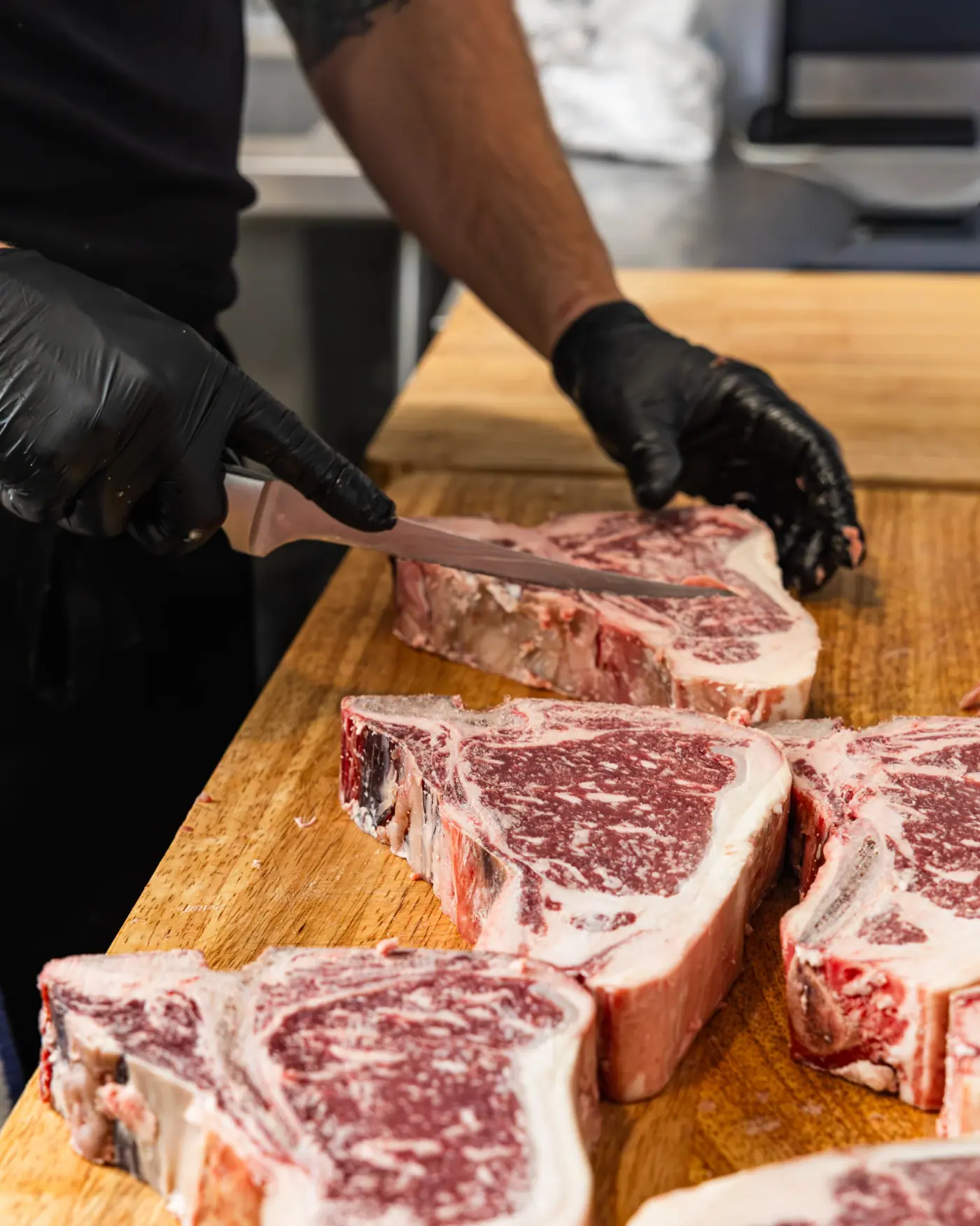 Gloved hands slicing a bone-in ribeye